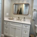 Bathroom vanity with white shaker doors, brass hardware, and quartz countertop