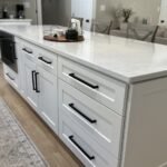 Kitchen island with white shaker drawers, black hardware, and quartz countertop