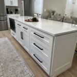 Kitchen island with white shaker drawers, black hardware, and quartz countertop