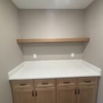 Maple cabinets with white countertop and floating shelf in a laundry nook